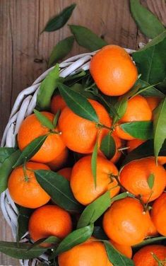 a basket filled with lots of oranges on top of a wooden table next to leaves