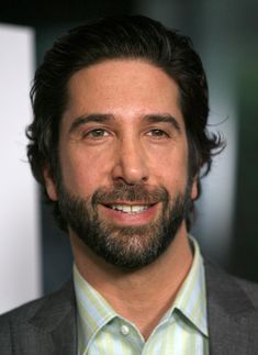 a close up of a person wearing a suit and smiling at the camera with a beard