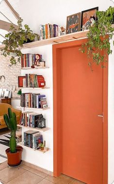 an orange door in a white room with bookshelves and plants on the shelves