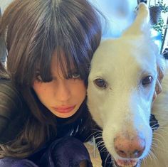 a woman hugging a white dog on top of her chest and looking at the camera