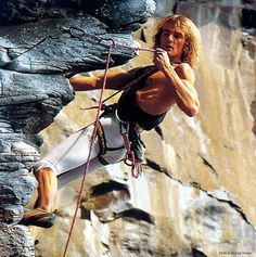 a man climbing up the side of a mountain with his hands on his hips and holding onto ropes