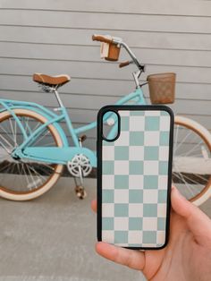 a person holding up an iphone case with a checkered pattern in front of a bicycle