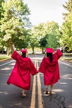 two women in red graduation gowns are walking down the street with their hands up