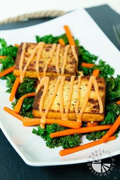 two pieces of tofu with sauce on top of some carrots and kale