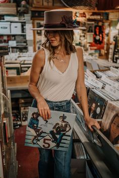 a woman in a hat is looking at some records on the shelf with her hands