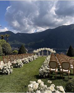 an outdoor ceremony set up with chairs and white flowers on the grass in front of mountains