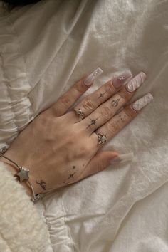 a woman's hand with three different rings and stars on her left wrist, sitting on a white sheet