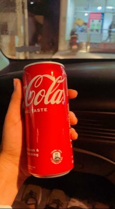 a hand holding a can of coca - cola in front of a car dash board