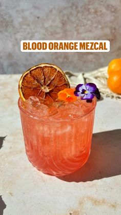 blood orange mezcal is garnished with an orange slice and purple pansies