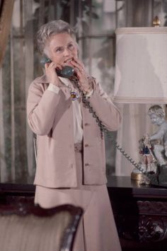 an older woman is talking on the phone in her living room while wearing a pink suit