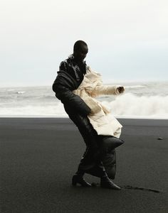 a man standing on top of a black sand beach next to the ocean with his foot in the air