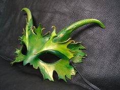 a green leafy mask sitting on top of a black leather couch