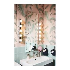 a bathroom with palm trees on the wall and mirror above it, along with two sinks