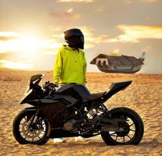 a person in yellow jacket standing next to a motorcycle on the beach with an airplane flying overhead