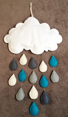 a white cloud with blue and gray rain drops hanging from it's side on the carpet