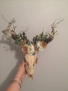 a deer skull with flowers and antlers on it's head is being held by a woman