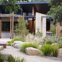 an outdoor area with rocks and plants in front of a house that is surrounded by trees