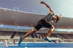 a male athlete is jumping in the air at an indoor track and field stadium on a sunny day