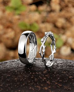 two wedding rings sitting next to each other on top of a wooden table with rocks in the background