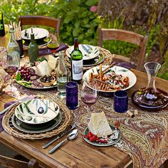 an outdoor table set with plates and wine bottles