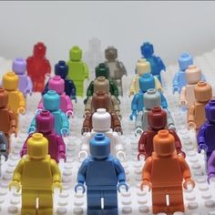 many different colored legos are arranged in a row on a white surface, with one person standing out from the crowd