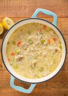 a bowl of soup with meat and vegetables on a wooden table next to lemon wedges