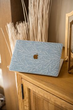 an apple laptop sitting on top of a wooden table next to a vase with dry grass