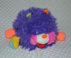 a purple and orange stuffed animal laying on top of a white surface with an orange nose