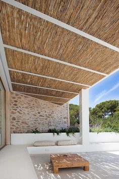 a wooden bench sitting under a roof next to a stone wall and grass covered area