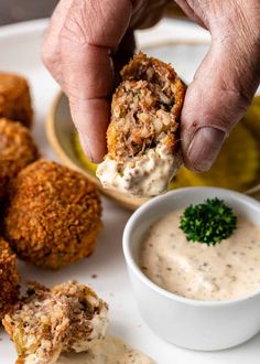 a person dipping something into a small white bowl with sauce on it and other food items in the background