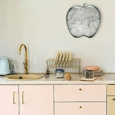 a kitchen with an apple shaped wall hanging above the sink and dishes on the counter