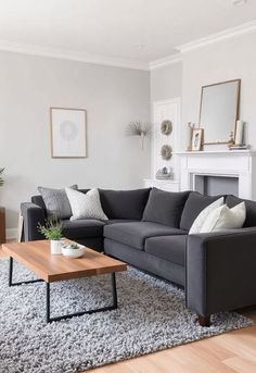 A cozy living room in soft shades of grey and white. The sofa is deep grey, adorned with textured pillows, while the walls are painted in a light grey tone. A wooden coffee table sits atop a grey shag rug, and there’s a stylish white fireplace with subtle decor accents. Grey And White Living Room, Grey Shag Rug, Textured Pillows, White Fireplace, White Living, White Living Room, Pillow Texture, Wooden Coffee Table