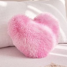 a pink heart shaped pillow sitting on top of a bed next to a white pillow