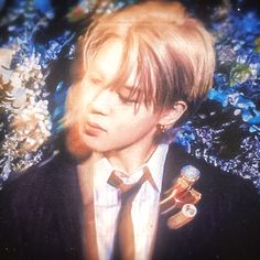 a young man with his eyes closed wearing a suit and tie, standing in front of blue flowers