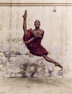 a man in a red feathered dress is dancing with his arms up and legs spread out