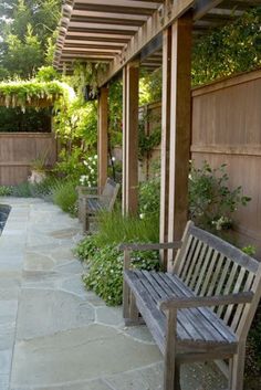 a wooden bench sitting under a pergoline covered patio next to a lush green yard