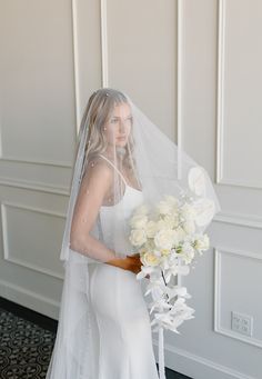 a woman in a white dress holding a bouquet of flowers and wearing a wedding veil