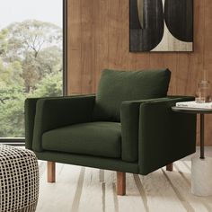 a green chair sitting in front of a window next to a table with a vase on it