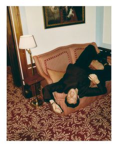 a man laying on top of a couch in a living room next to a lamp