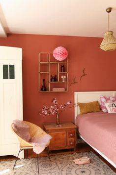 a bedroom with a bed, chair and pink walls in the corner is decorated with decorative items