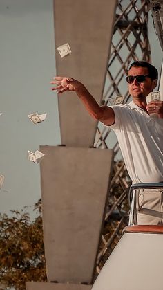 a man in white shirt and sunglasses throwing money into the air on top of a boat