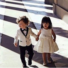 two young children dressed in formal wear holding hands and walking down the street with their arms around each other