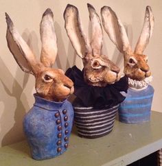 three statues of rabbits in top hats on a shelf