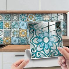 two hands holding up a photo in front of a kitchen counter with blue and white tiles