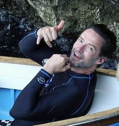 a man sitting in a boat pointing to something on the side with his finger up