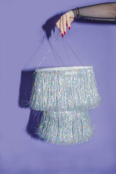 a woman's hand holding a chandelier in front of a purple wall