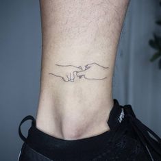 a tattoo on the ankle of a person with two hands touching each other's fingers