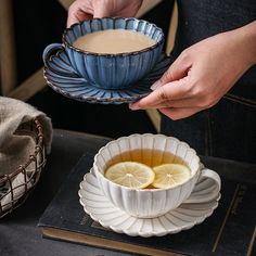 a person holding a tea cup and saucer over a bowl filled with lemon slices