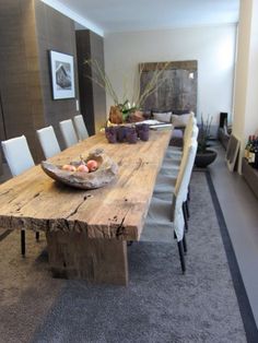 a large wooden table with white chairs and fruit on it in the middle of a room