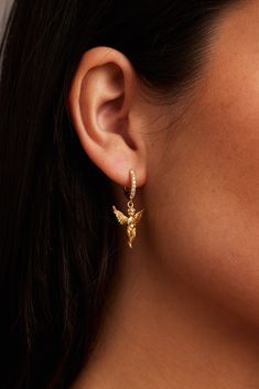 a close up of a woman's ear wearing gold earrings with an angel design